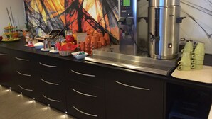 A buffet setup with a coffee machine, various food items, and a decorative wall.