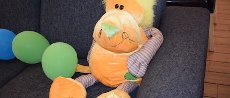 Un león de peluche sobre un sofá gris, cerca hay globos azules y verdes.