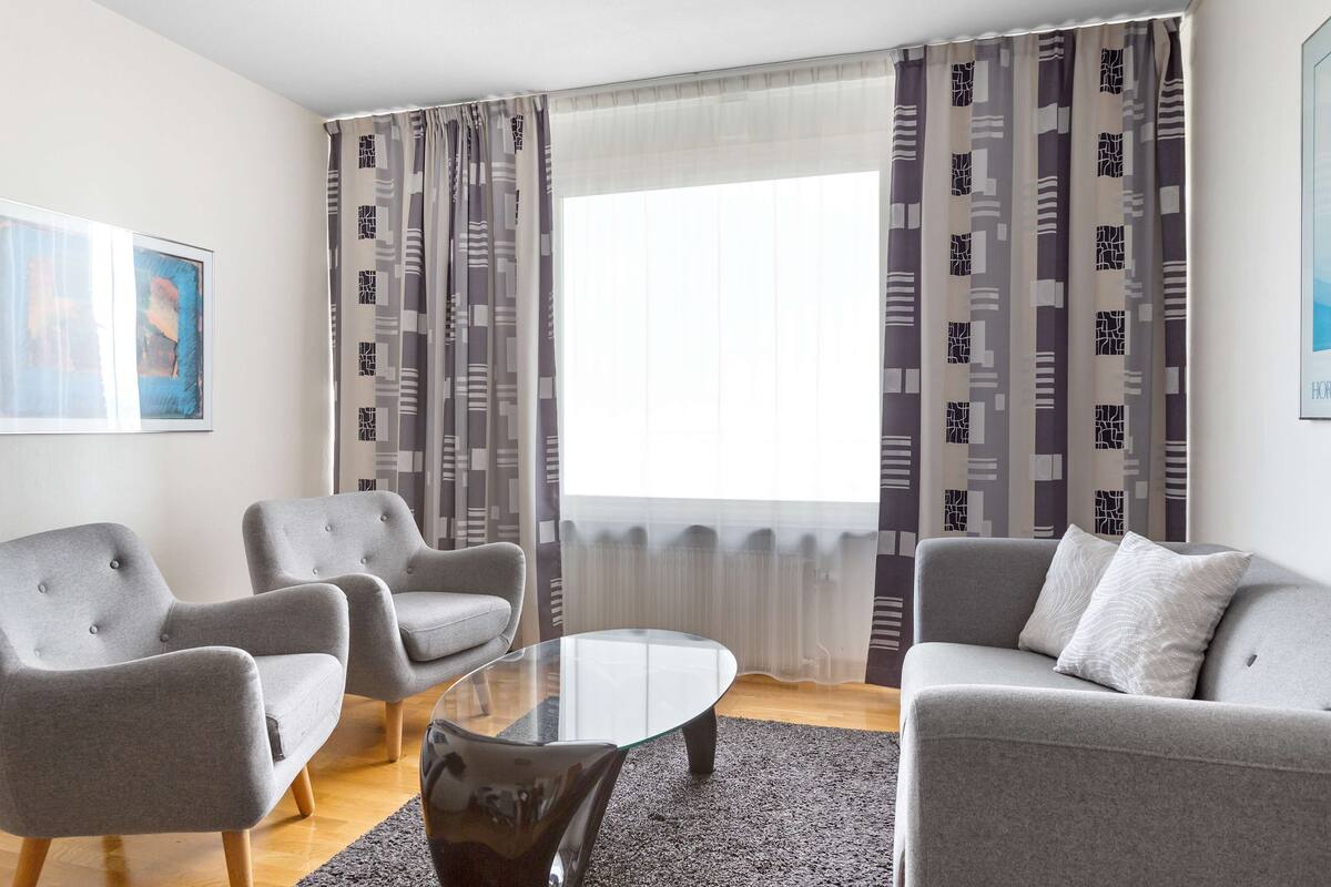 A modern living room with a grey sofa, two armchairs, and a glass coffee table.