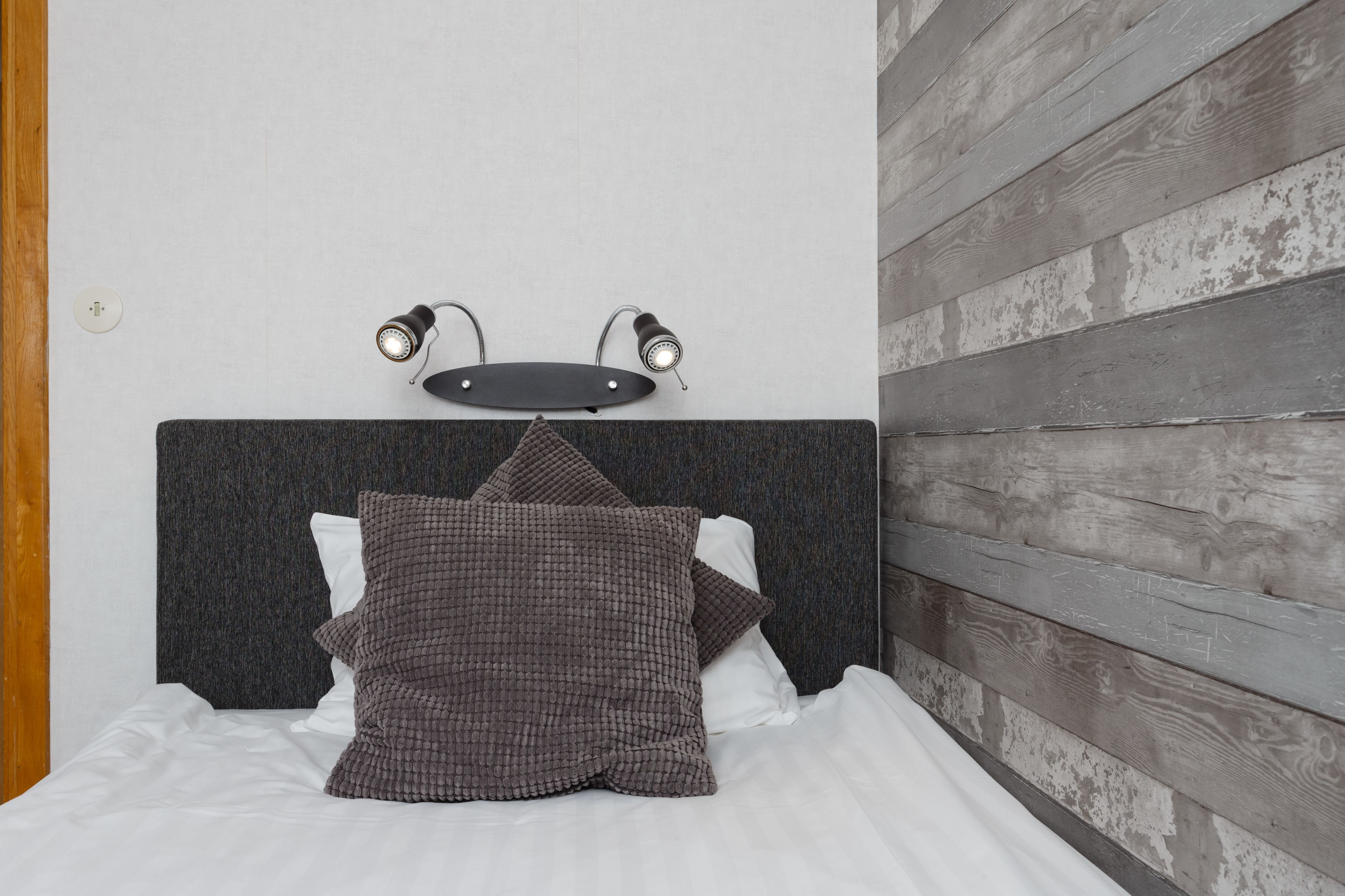 A bed with a dark headboard, two wall-mounted lights, and a wooden wall panel.