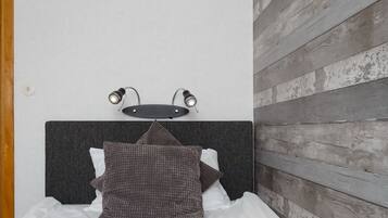 A bed with a dark headboard, two wall-mounted lights, and a wooden wall panel.