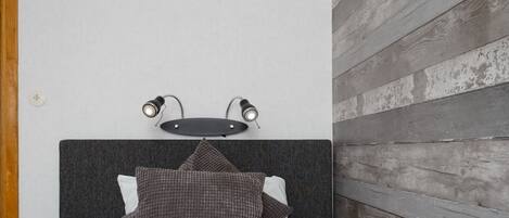 A bed with a dark headboard, two wall-mounted lights, and a wooden wall panel.