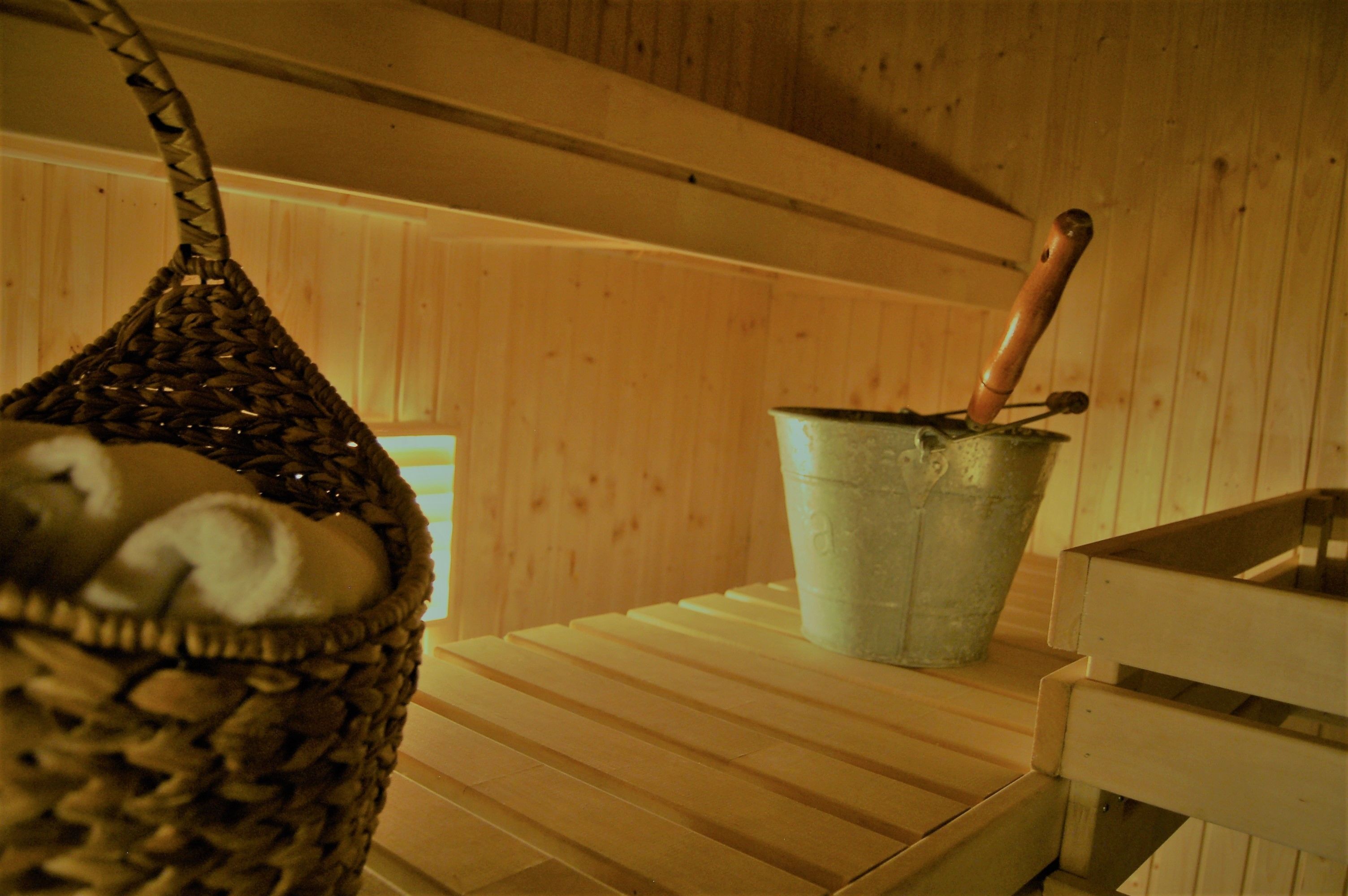 Una sauna de madera con una cesta tejida y un cubo de metal con asa de madera.