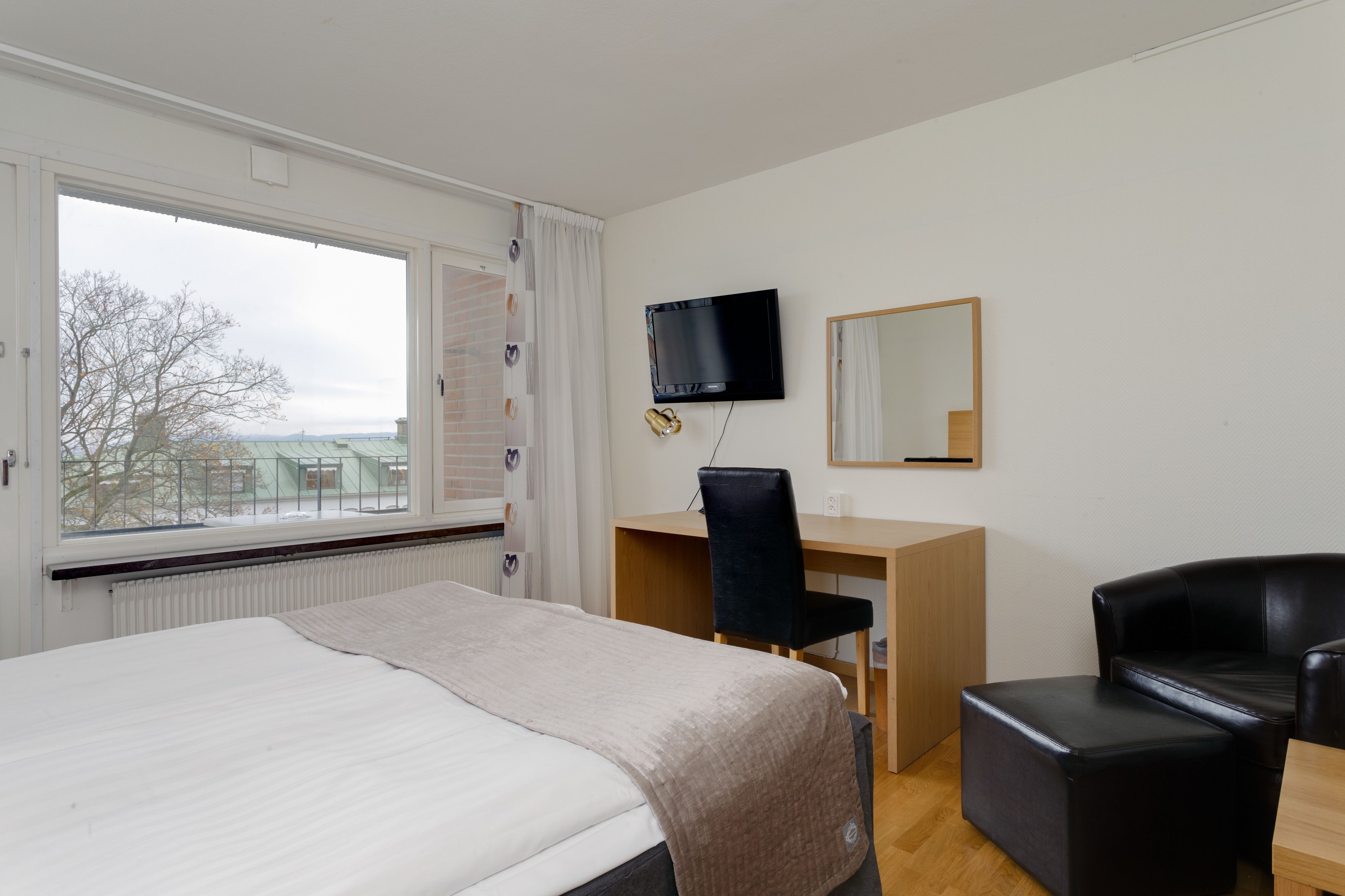 Una habitación de hotel con una cama, un escritorio con una silla, un televisor y un espejo.
