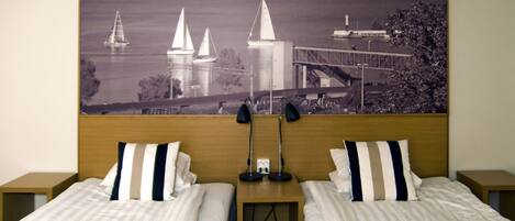 A hotel room with two beds, a large window with a scenic view of a bridge and sailboats, and a wooden headboard.