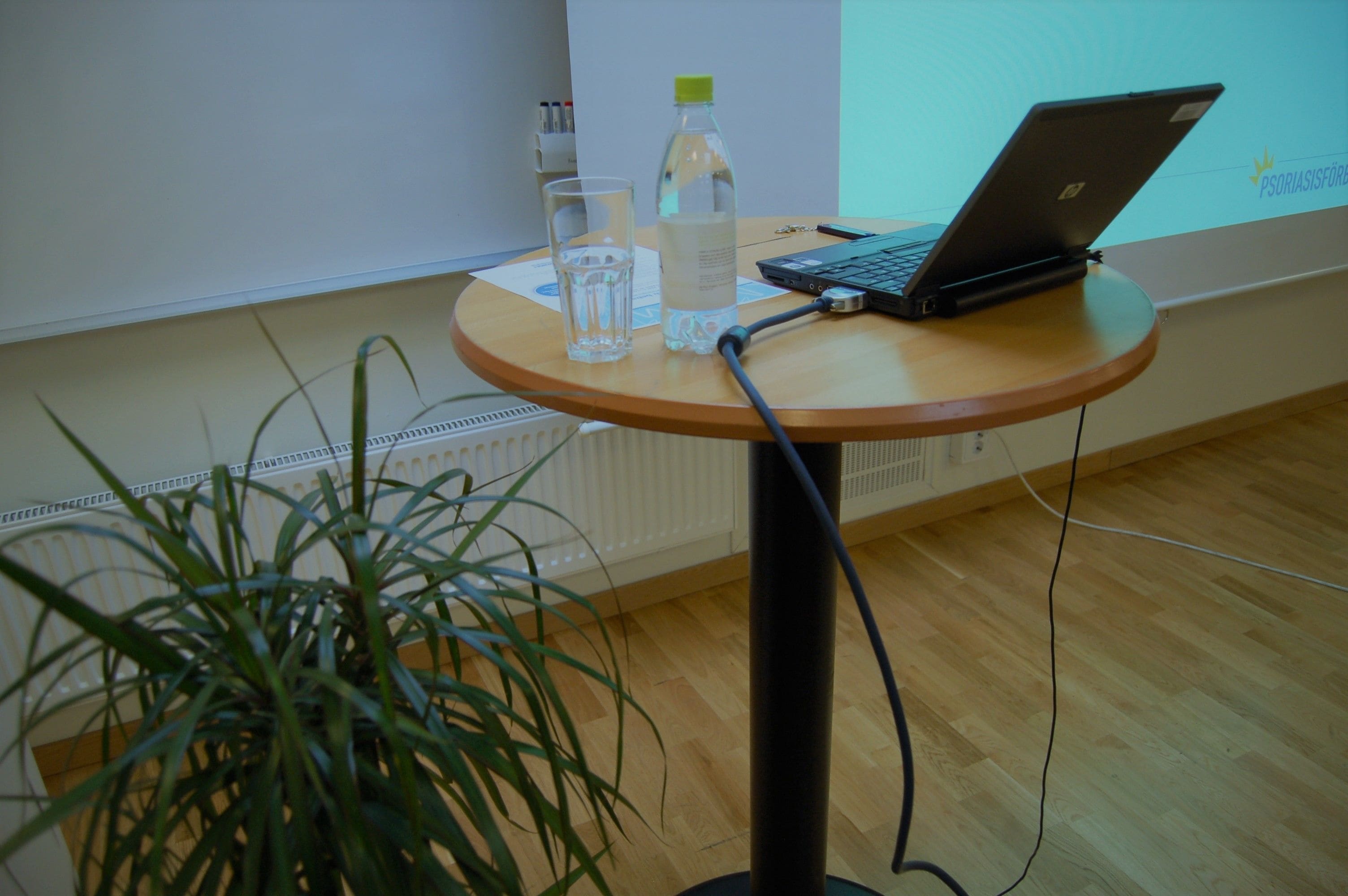 Un ordinateur portable est posé sur une table en bois, à côté d’une bouteille et d’un verre.