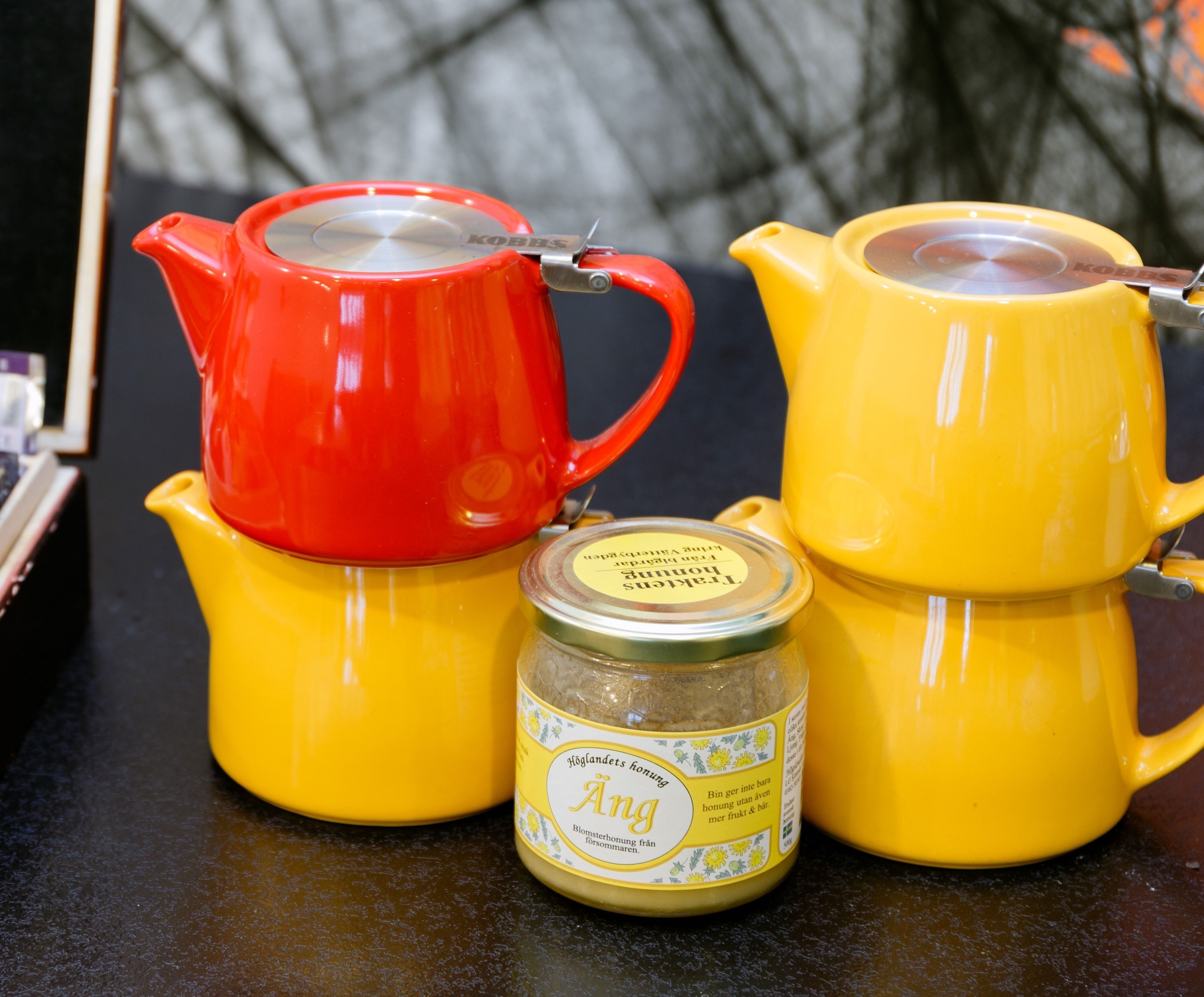 Three yellow teapots and a red teapot with a lid, placed on a dark surface.