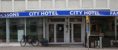 Un hotel urbano con entrada despejada, una bicicleta estacionada afuera y una maceta con flores.