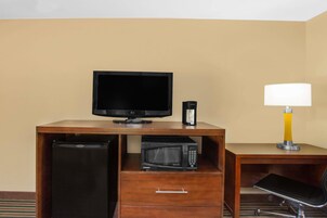 Habitación de hotel con escritorio de madera, televisor, microondas, refrigerador y lámpara.