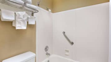 A bathroom with a white bathtub, a toilet, a towel rack with folded towels, and a handrail.