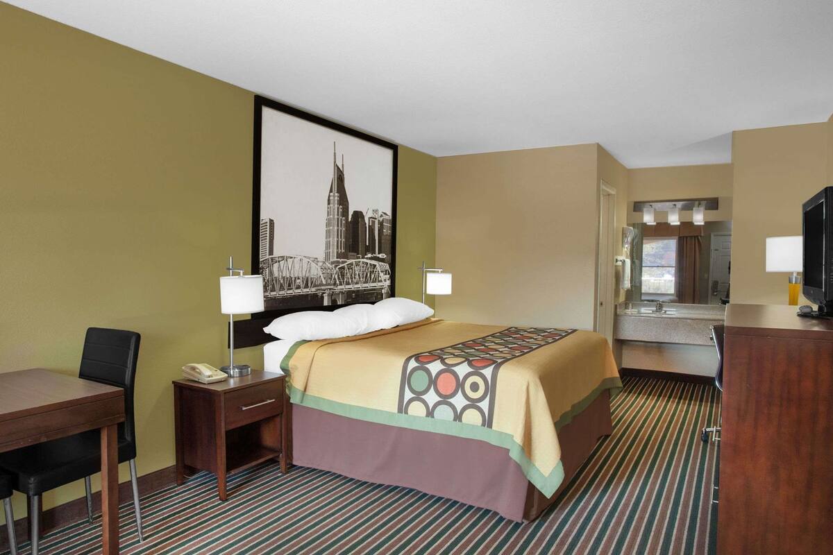 Ein Hotelzimmer mit Bett, Schreibtisch, Stuhl, Telefon, Fernseher und einem durchgegangenen Tür sichtbaren Badezimmer.