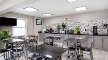 A modern kitchen with a coffee station, dining tables, and chairs.