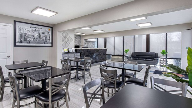 A modern dining area with multiple tables and chairs, a kitchen area, and large windows providing natural light. - Super 8 by Wyndham Nashville West (Nashville)