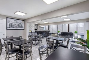 A modern dining area with multiple tables and chairs, a kitchen area, and large windows providing natural light.