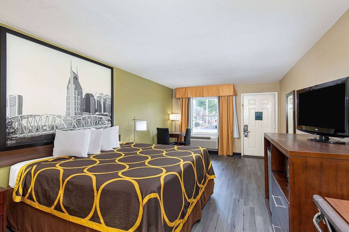 Ein Hotelzimmer mit Bett, Schreibtisch, Fernseher, einer Tür und einem Fenster mit Vorhängen.
