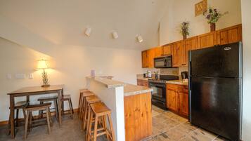 A kitchen with wooden cabinets, a black refrigerator, a microwave, and a bar area with stools.