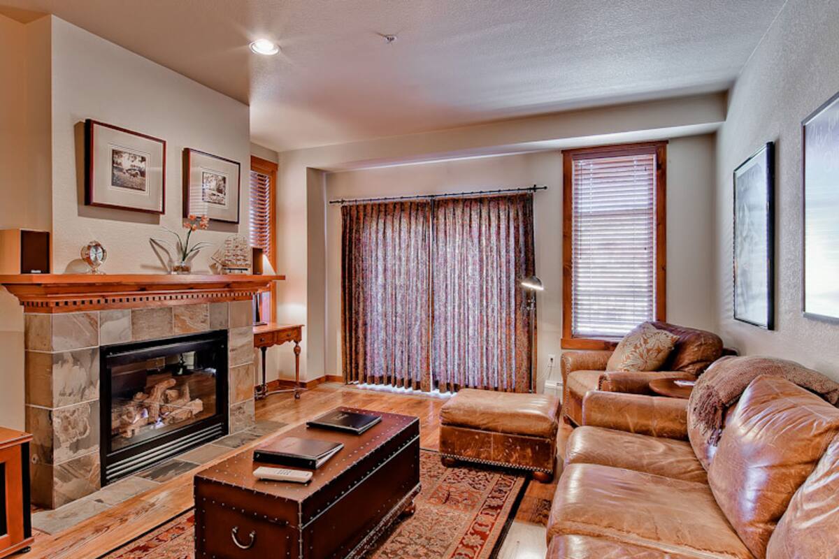 A living room with a fireplace, leather sofa, and a large window with curtains.