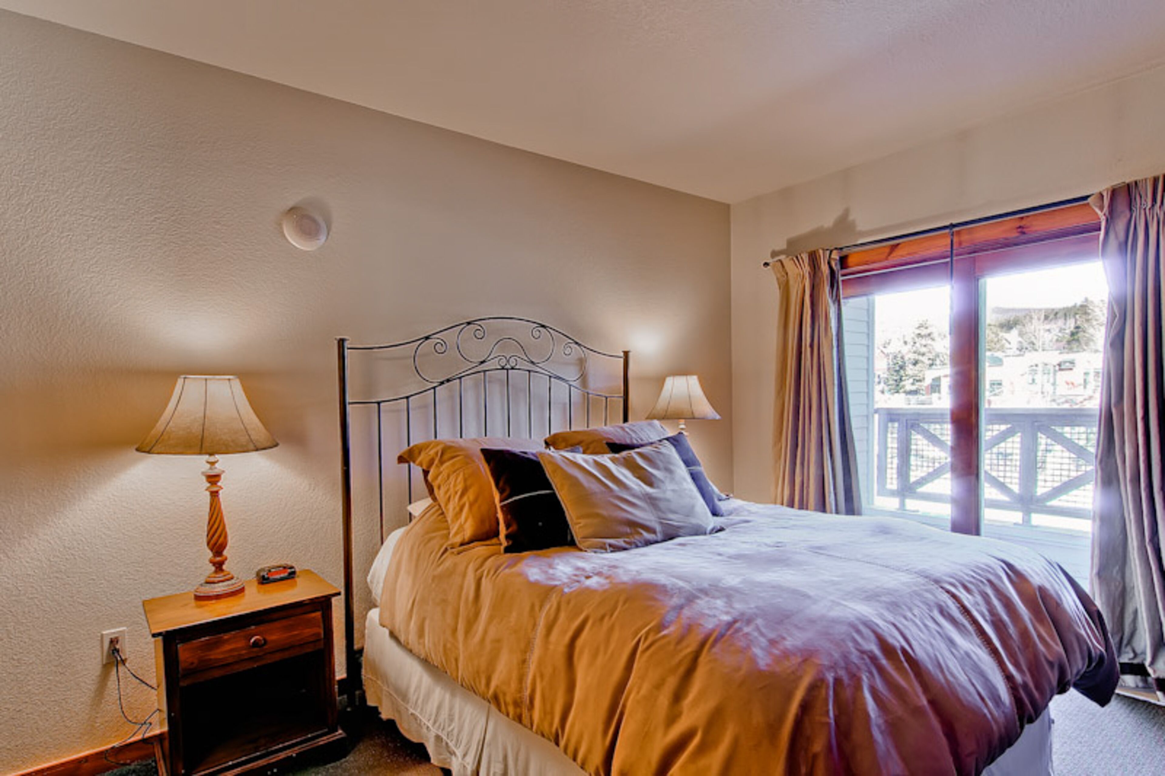 A bedroom with a bed, two bedside lamps, a nightstand, and a window with curtains.