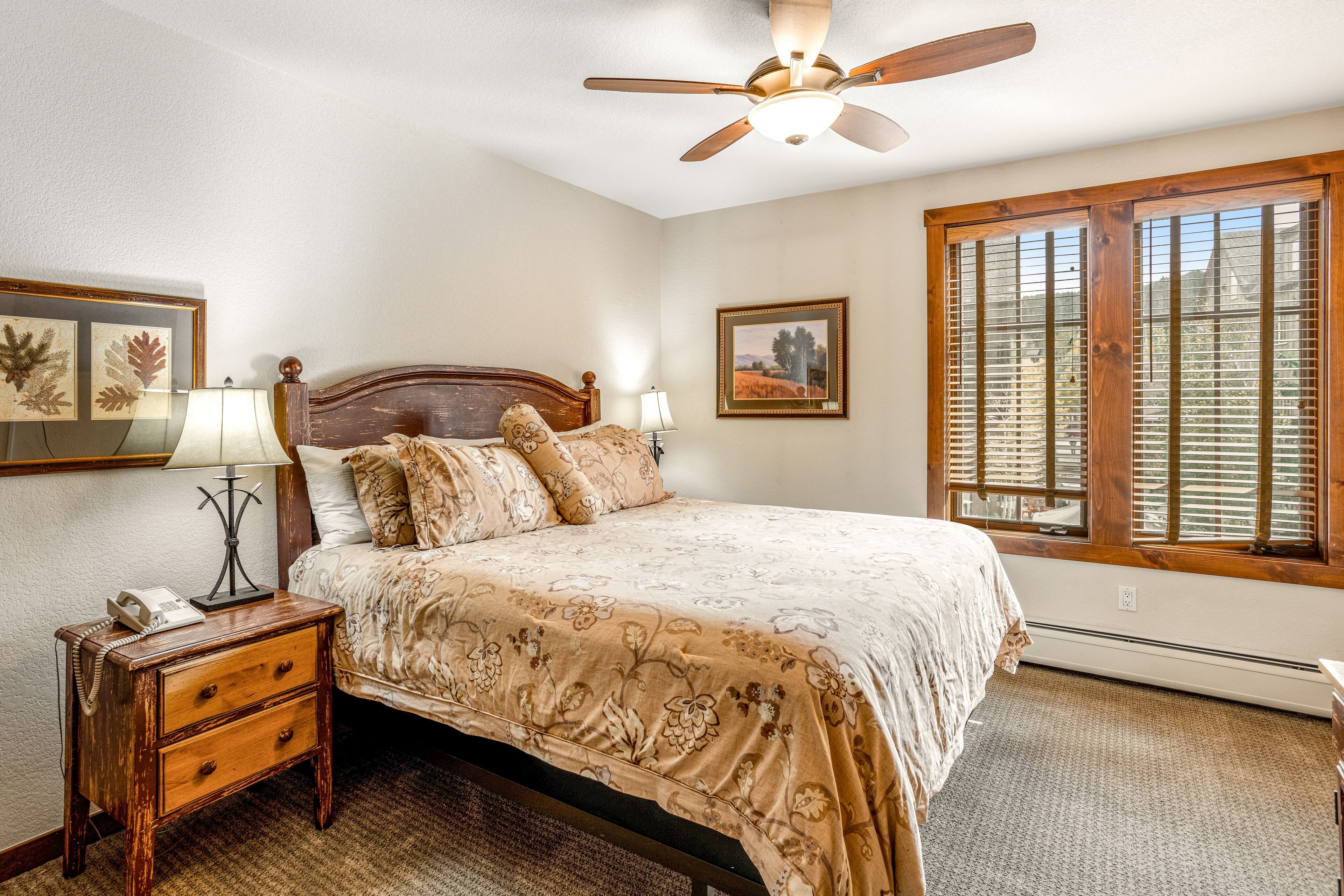 A bedroom with a wooden bed, a nightstand with a lamp, and framed pictures on the wall.
