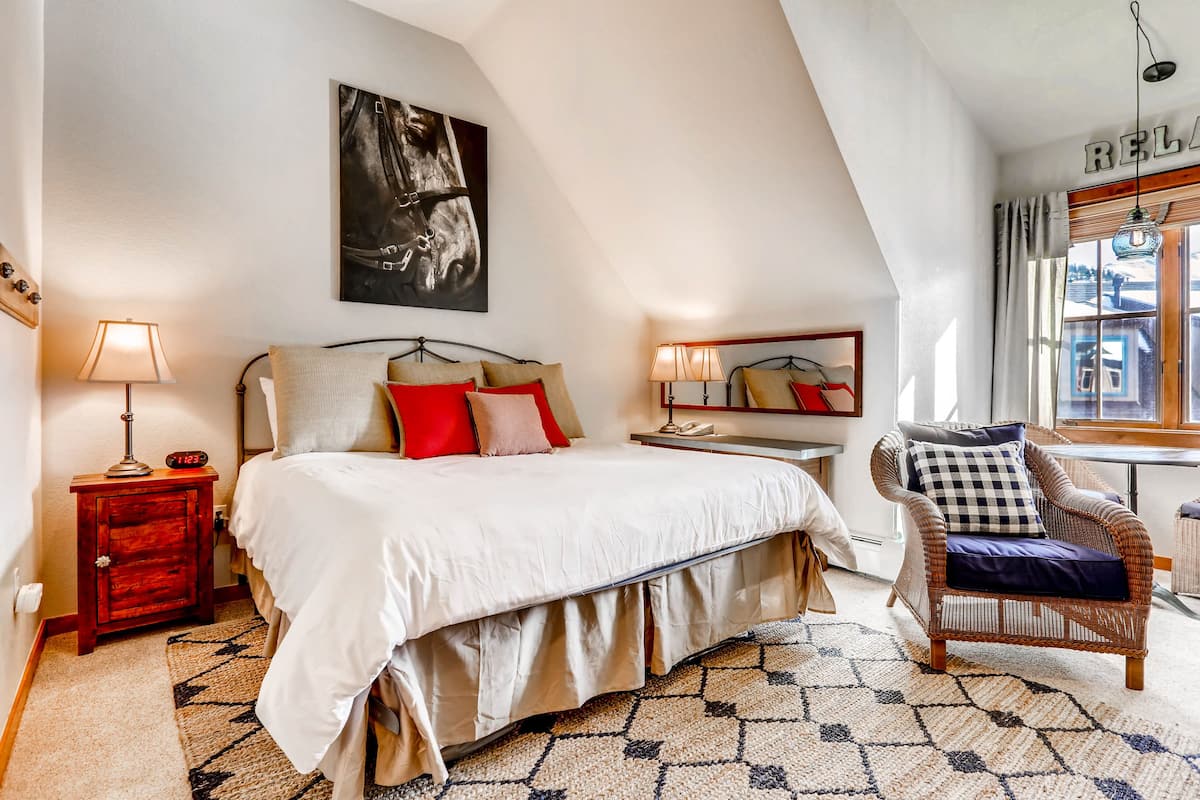 A bedroom with a bed, bedside lamps, a chair, a rug, and a painting on the wall.