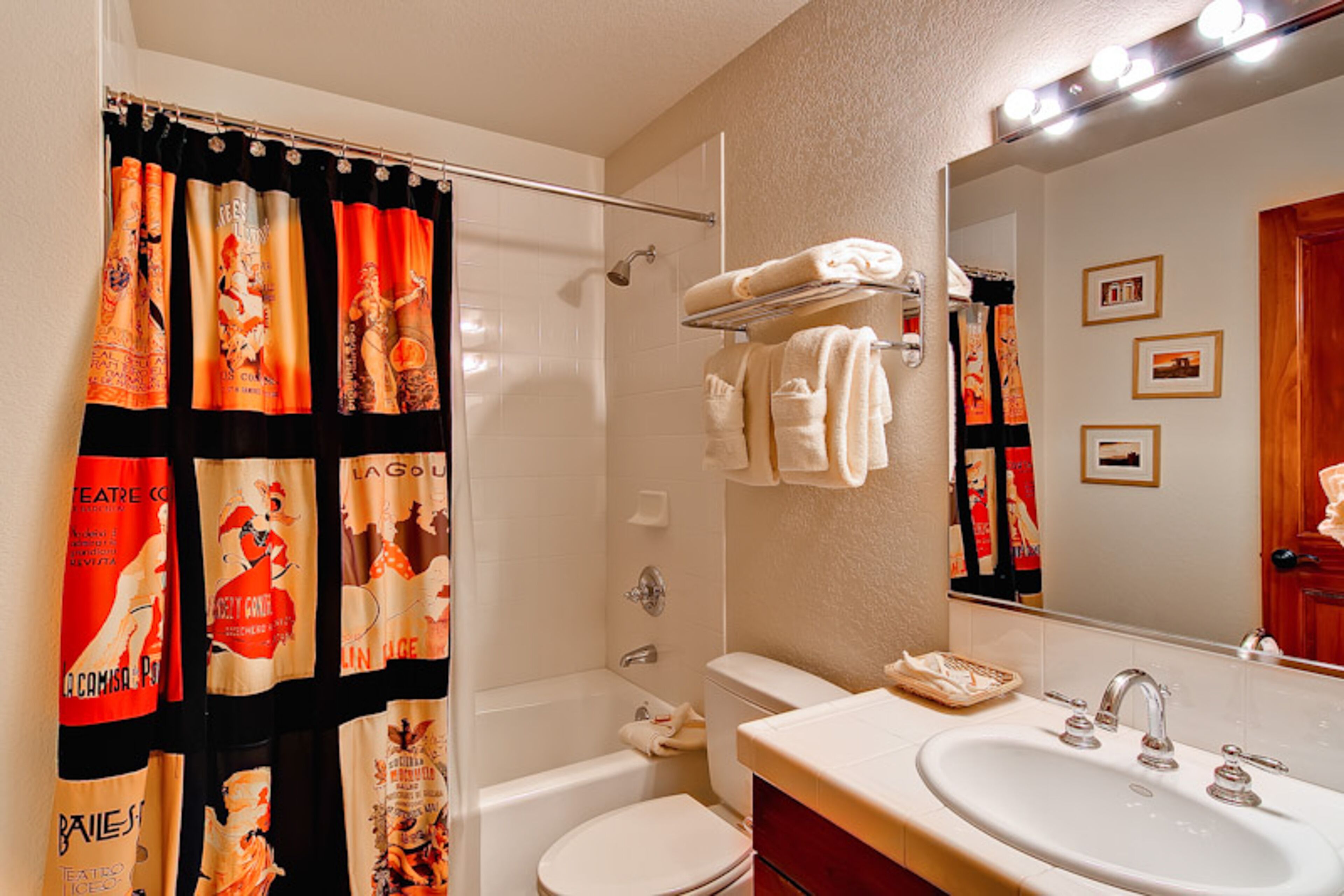 A bathroom with a shower curtain featuring theater posters, a bathtub, a toilet, a sink with a mirror, and a towel rack.