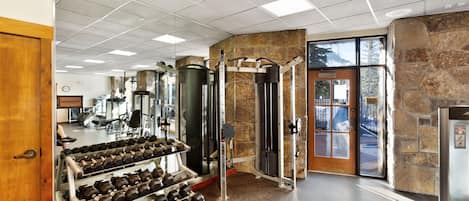 A gym with weightlifting equipment, a mirror, and a stone wall.