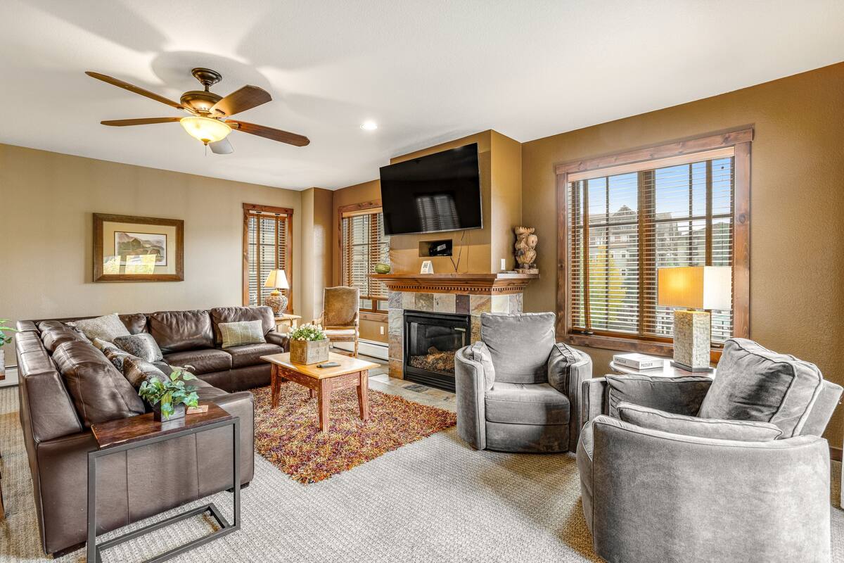 A living room with a fireplace, leather sofas, a television, and a ceiling fan.