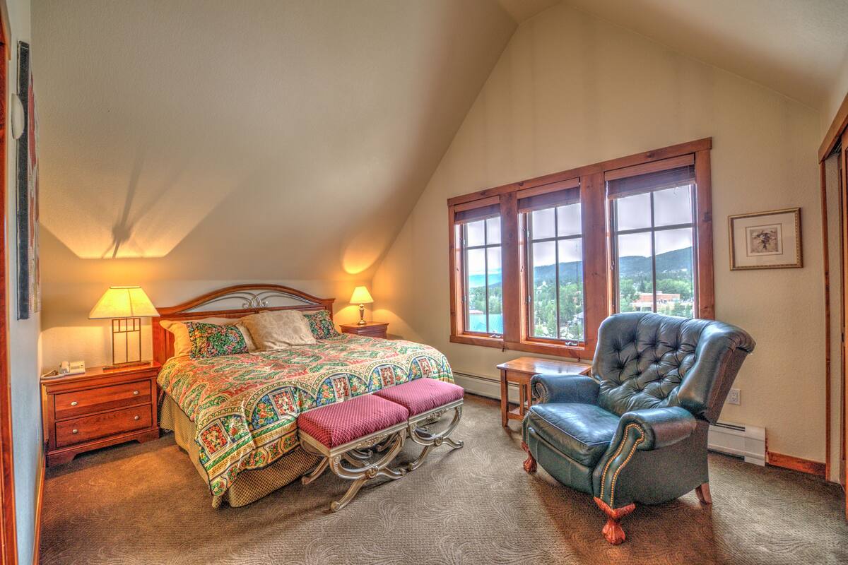 A bedroom with a large bed, a chair, a nightstand, and a window with a view.