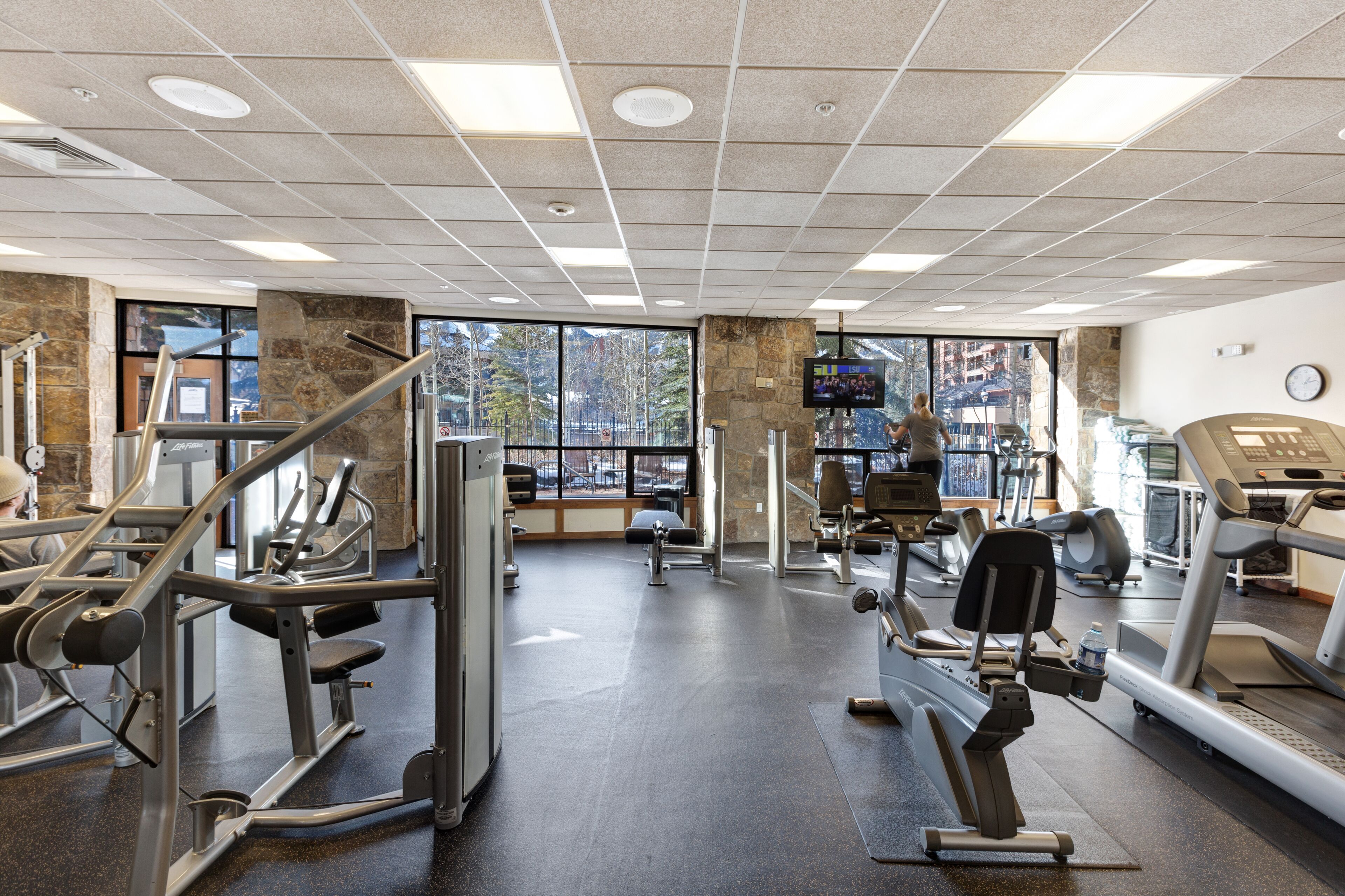 Un gimnasio con diverso equipo de ejercicio, amplias ventanas y un pilar de piedra.