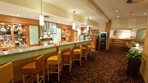 Un espace bar doté d ’un long comptoir, de nombreux tabourets, ainsi que d’une grande variété de bouteilles et de verres.