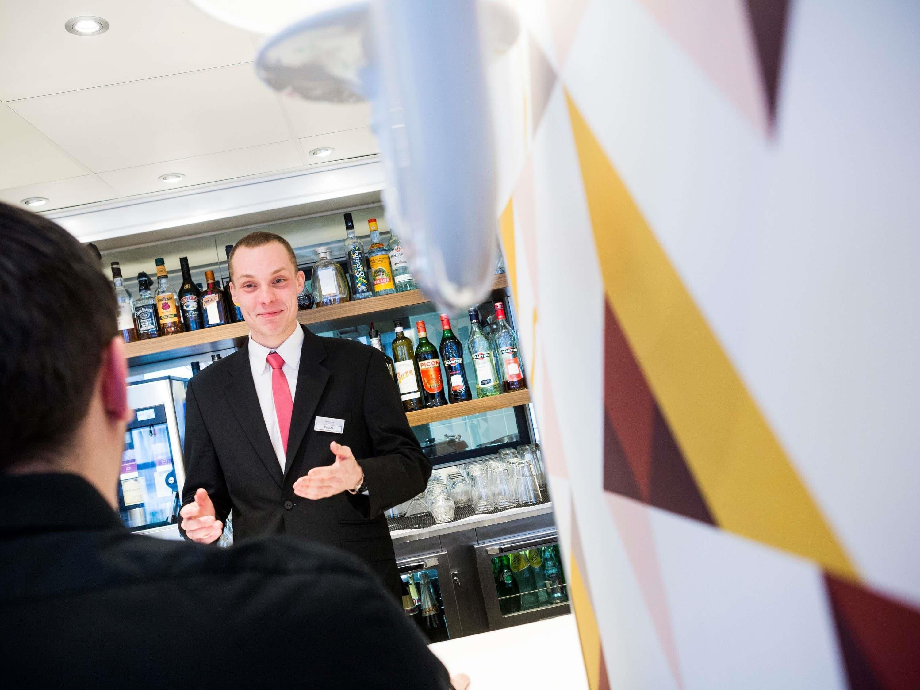A bar area with shelves stocked with various liquor bottles, a bar counter, and a person in a suit.
