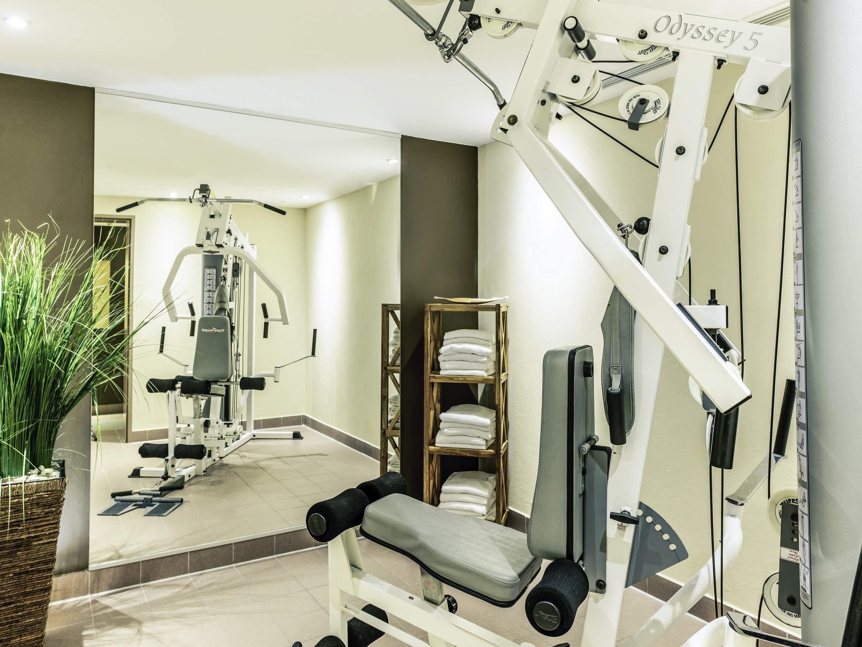 Un gimnasio con equipo de ejercicio, un espejo, una planta y un estante con toallas.