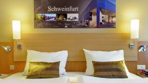 A hotel room with two beds, a wooden headboard, and a wall-mounted poster of Schweinfurt.
