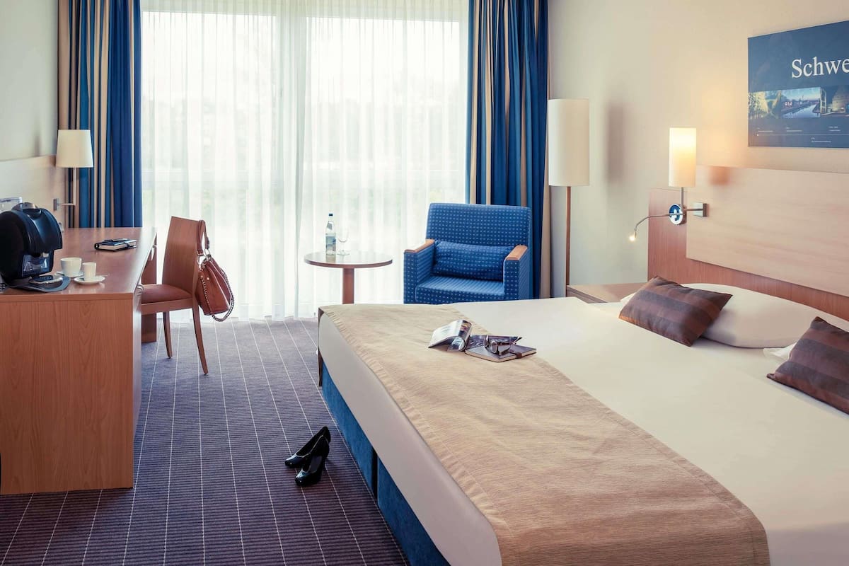 Een hotelkamer met een bed, een bureau, een stoel, een klein tafeltje en een lamp.