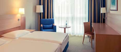 A hotel room with two beds, a desk, a chair, a small table, and a large window with curtains.