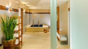 Une salle de bain moderne avec une baignoire, une étagère en bois où sont posées des serviettes et une grande plante en pot.