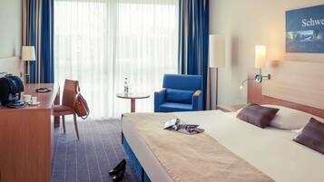 Una habitación de hotel con cama, escritorio, silla, mesita y lámpara.