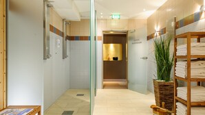 Une salle de bain moderne avec des parois de douche en verre, un banc en bois, un porte-serviettes et une plante.