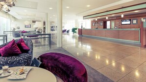 Un hall d’hôtel moderne avec un comptoir d’accueil, un espace salon et une table à manger agrémentée d’un canapé violet et d’une assiette de nourriture.
