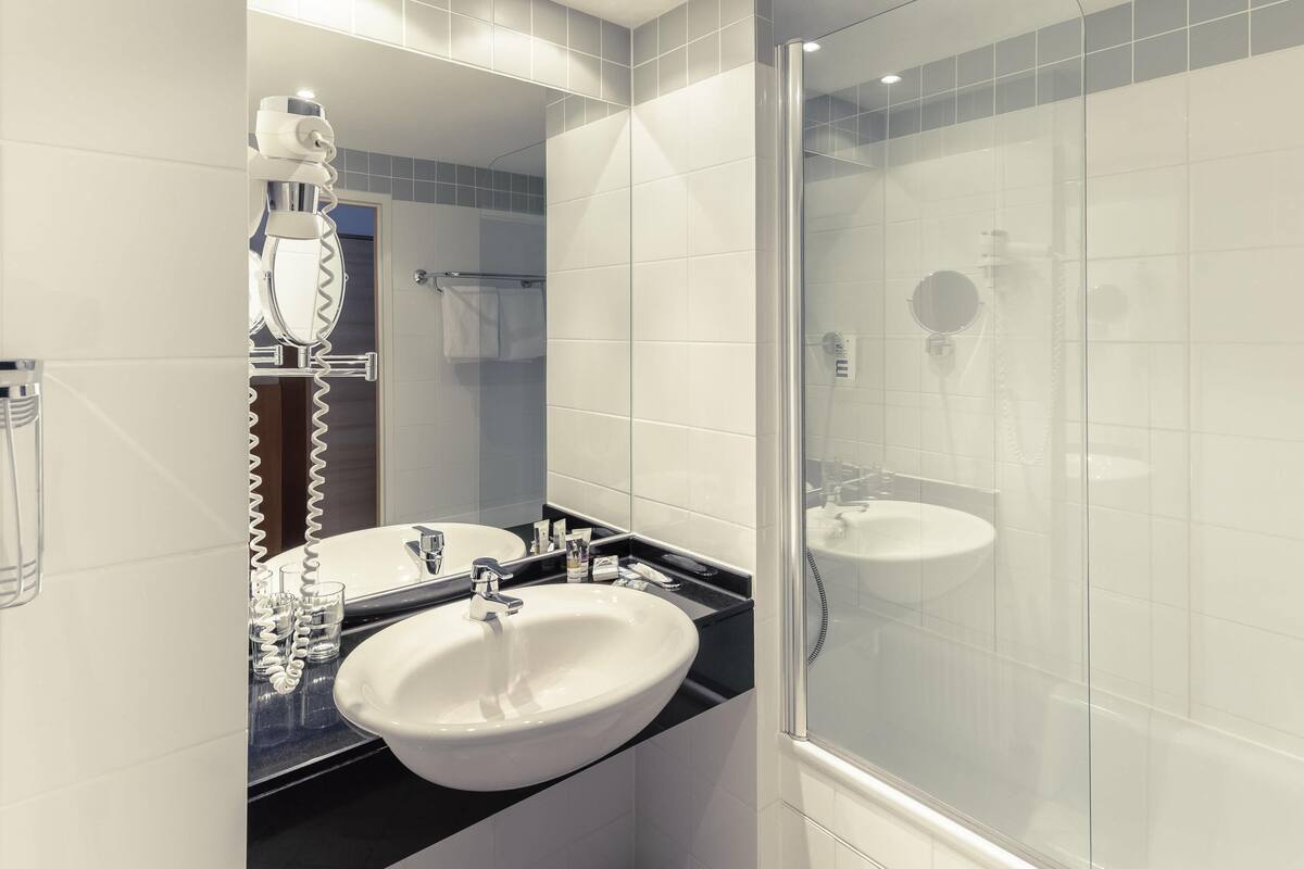 Un baño moderno con ducha de vidrio, un lavamanos blanco y un espejo.