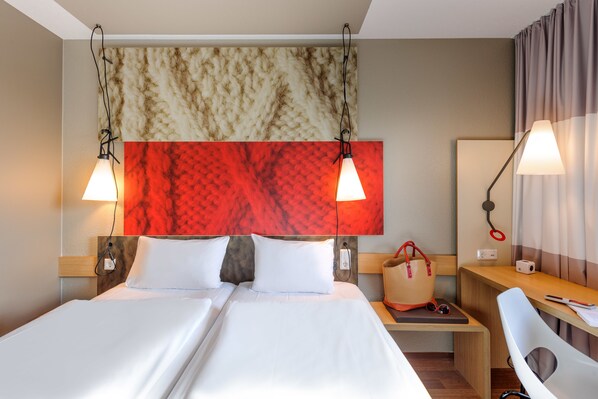 A hotel room with a double bed, two bedside lamps, a wooden nightstand, a chair, and a desk with a lamp.