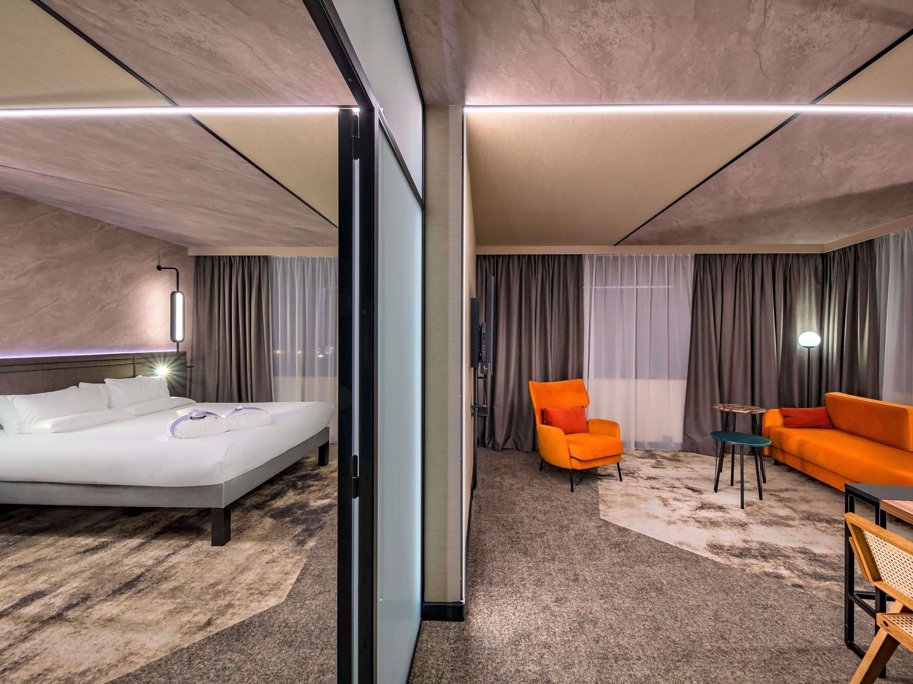 A hotel room with a bed, a sofa, a chair, a small table, and a TV.