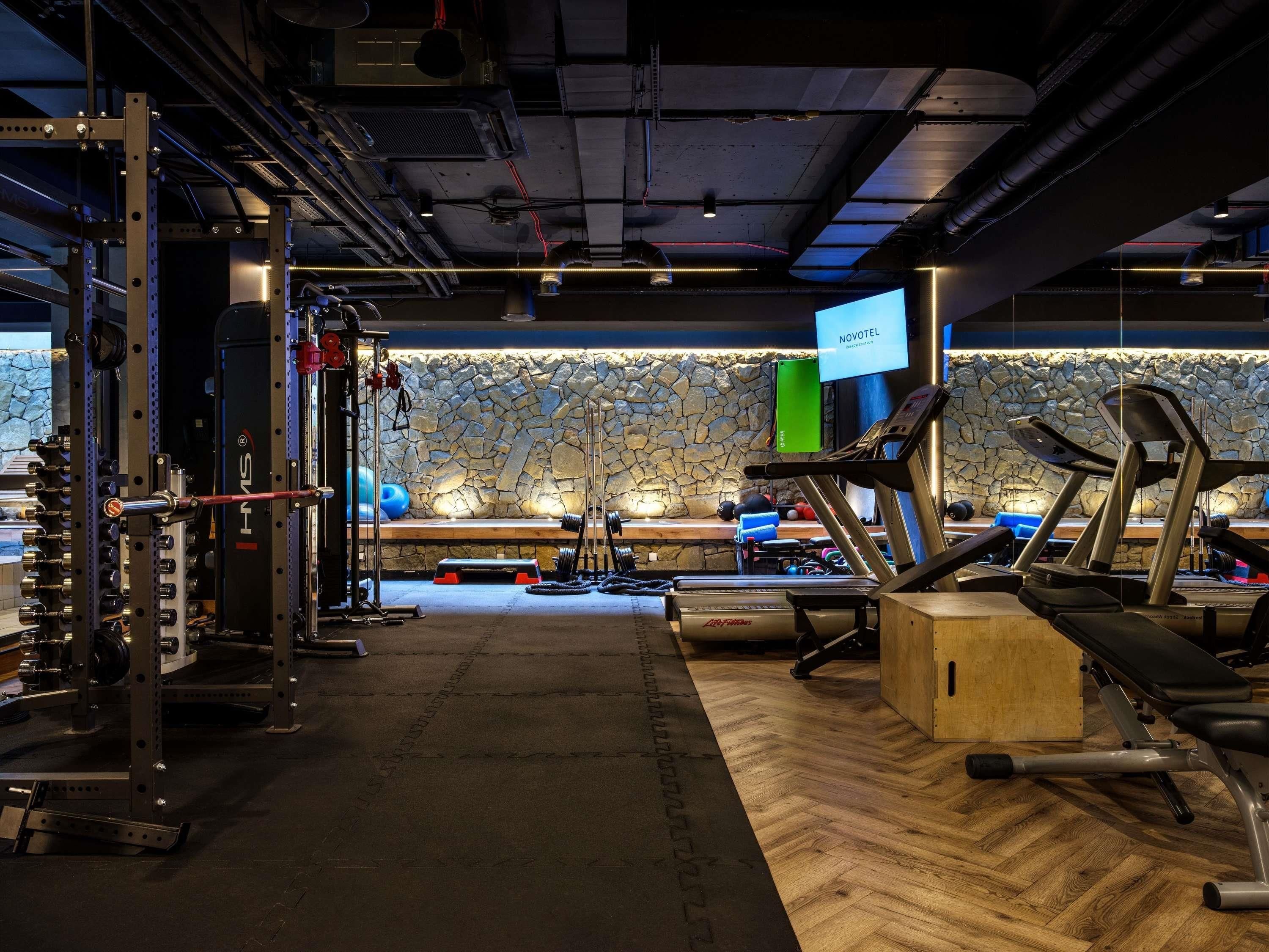 A gym with weightlifting equipment, treadmills, and a stone wall.