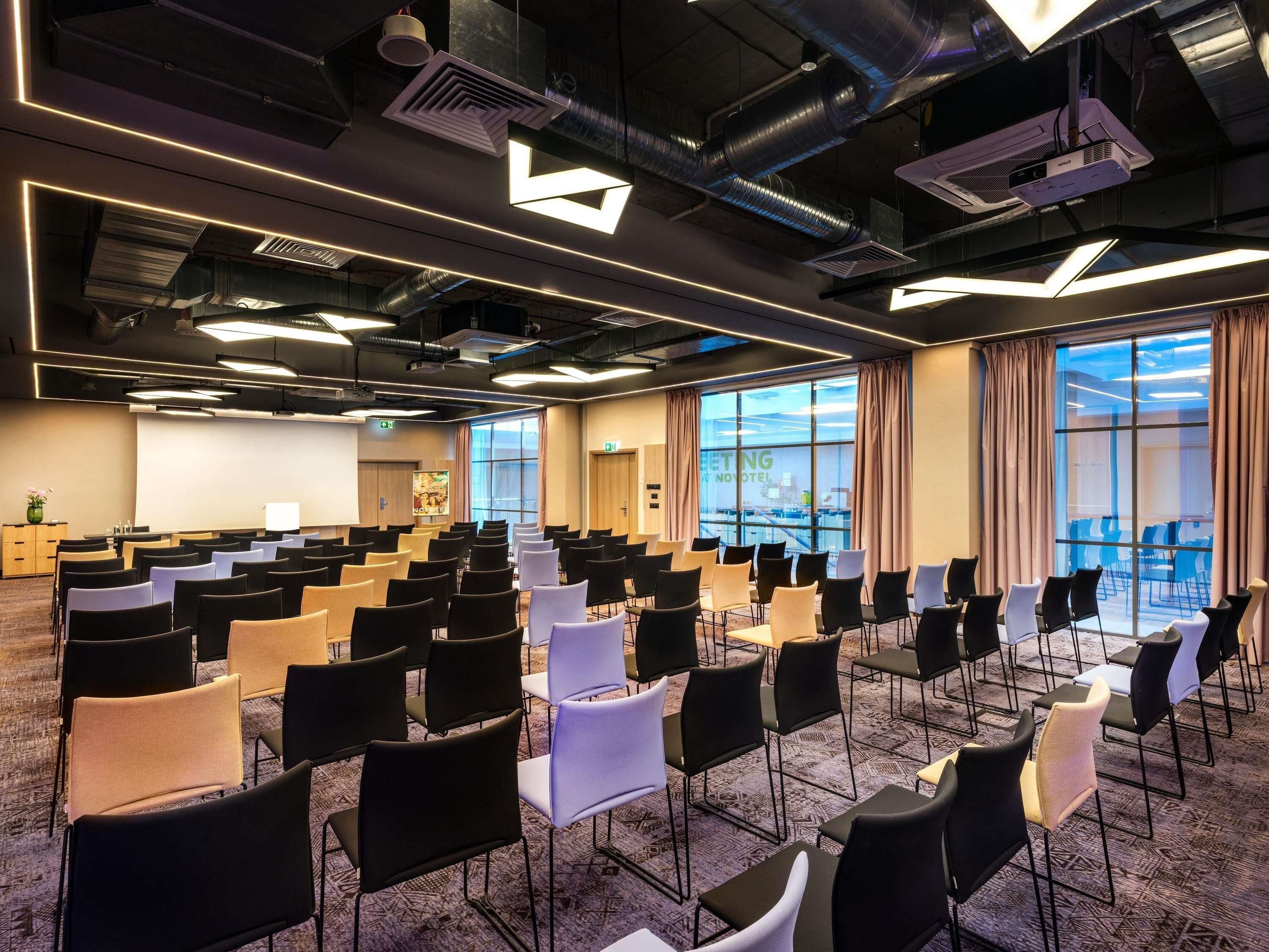 A conference room with rows of chairs, a projector, and a large window with curtains.