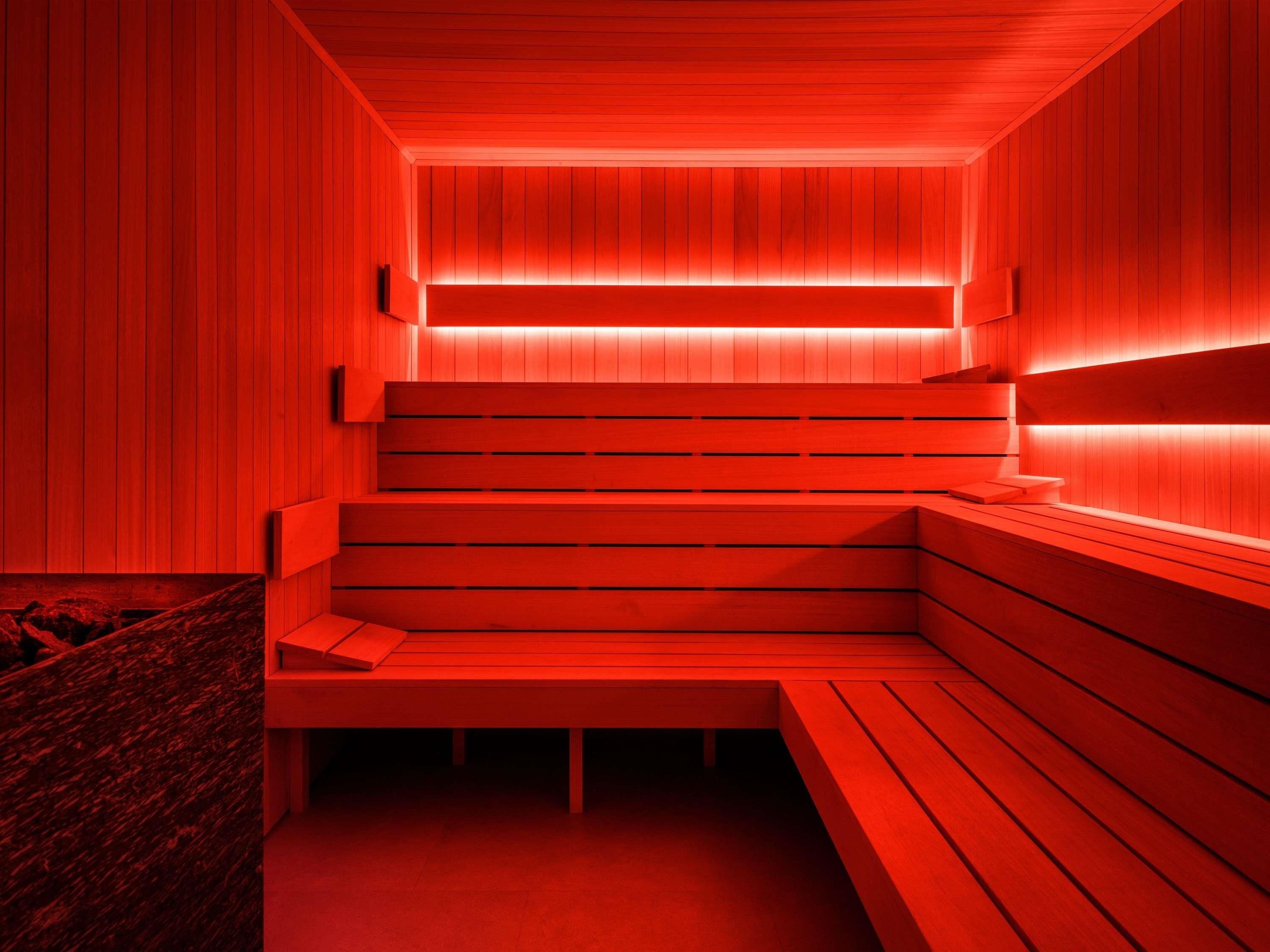A red-lit sauna with wooden benches and a bench at the bottom.