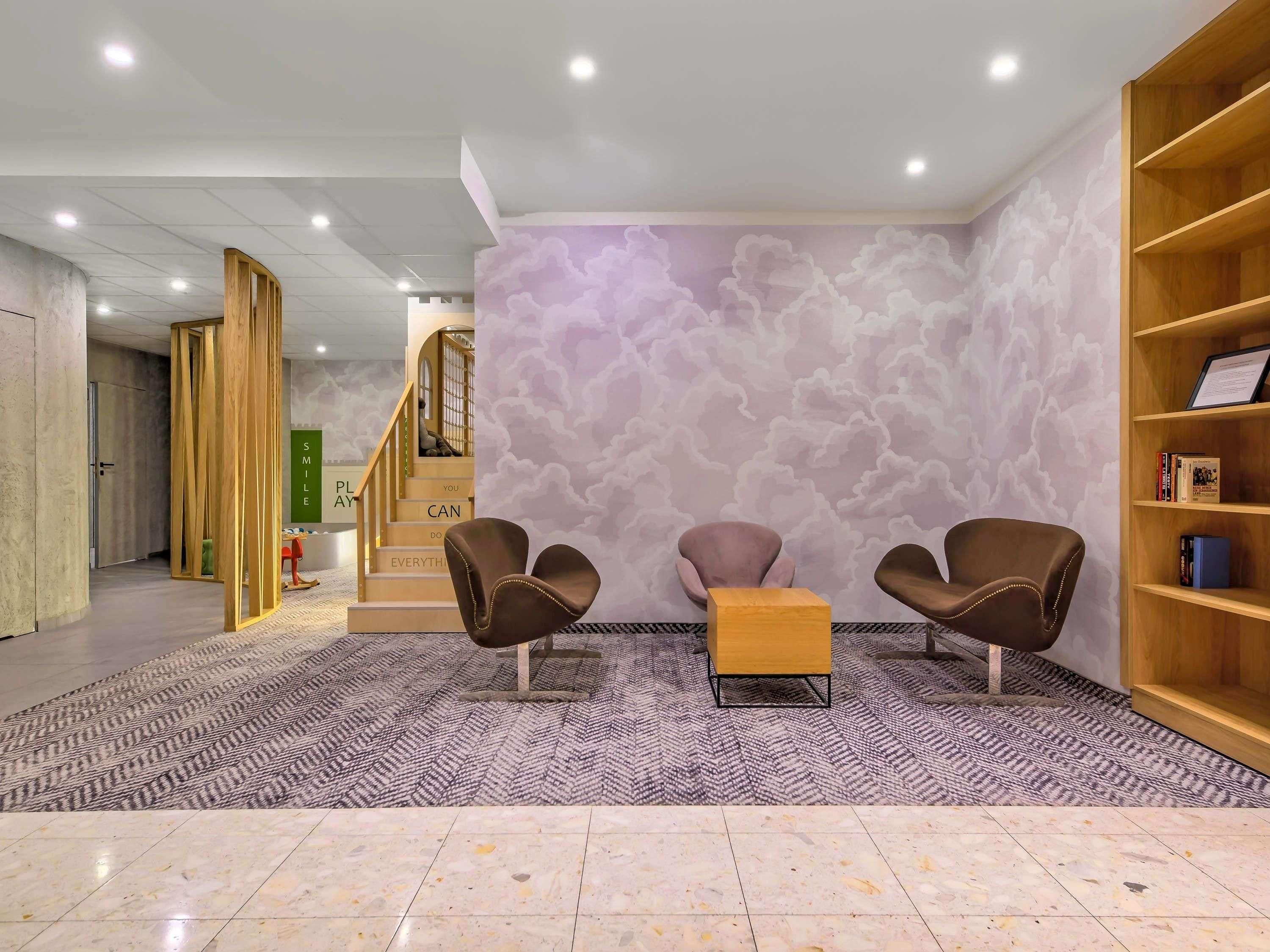 A lobby with a staircase, two leather chairs, a wooden bookshelf, and a patterned carpet.