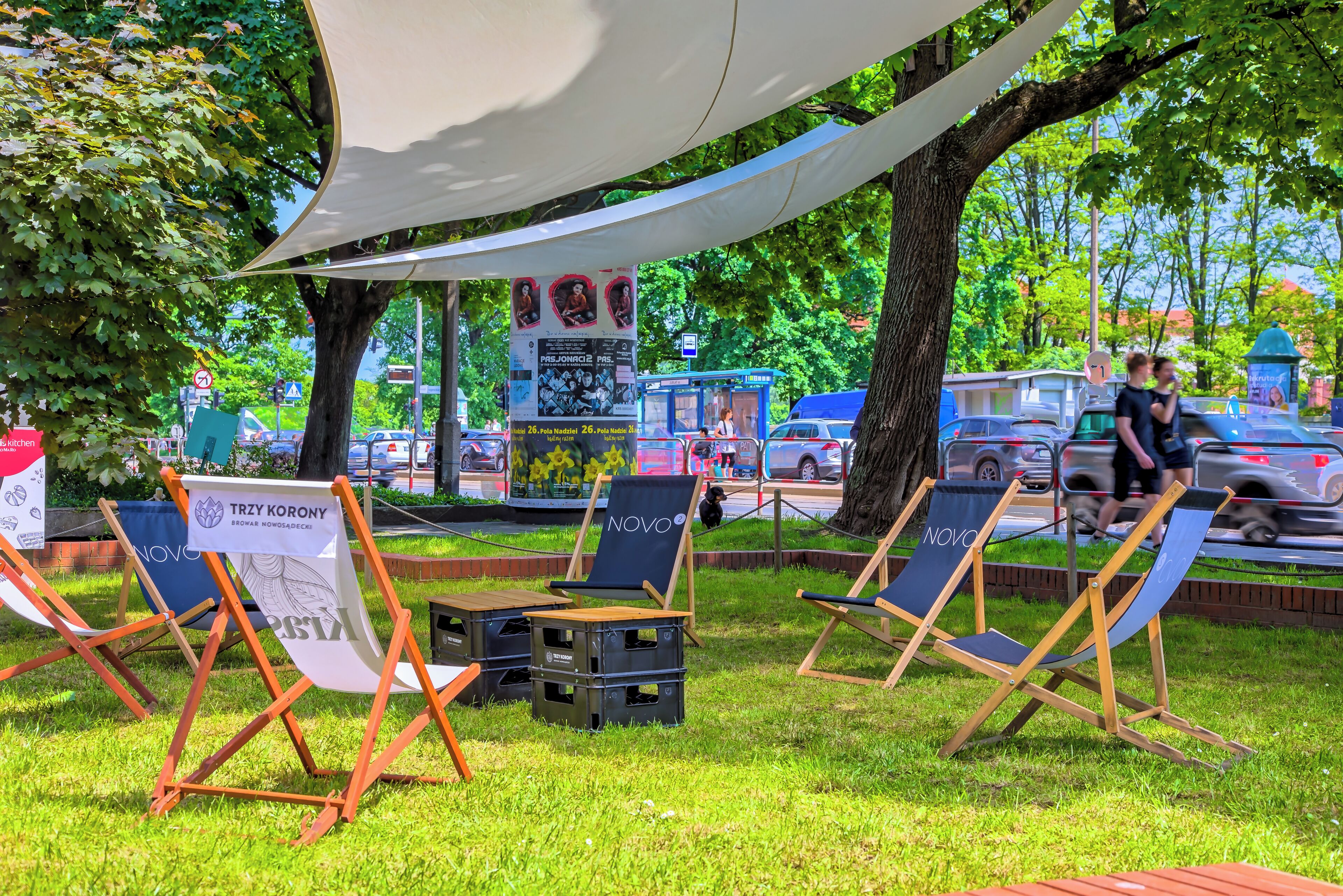 Outdoor seating with a banner advertising an event, a bus stop, and a tree-lined street.