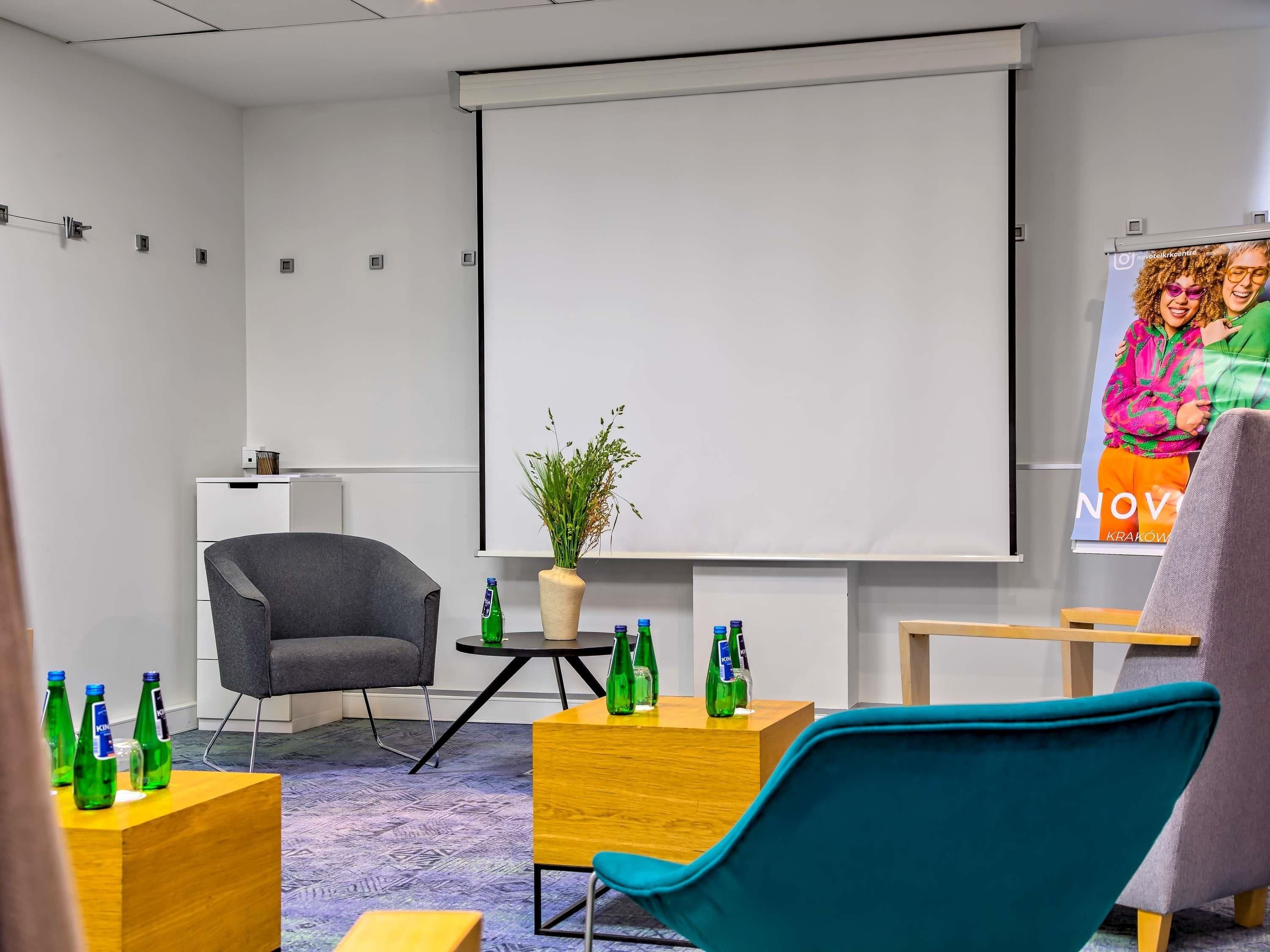 Une salle de conférence équipée d’un écran de projection, d’une petite table ornée d’une plante en pot et de plusieurs chaises.