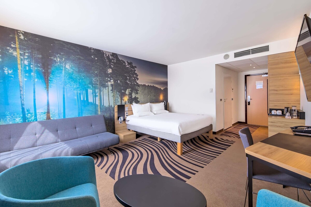 A hotel room with a bed, a sofa, a small round table, and a dining table.