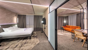 A modern hotel room with a bed, a desk, an orange sofa, and a TV. - Novotel Krakow Centrum (Kraków)
